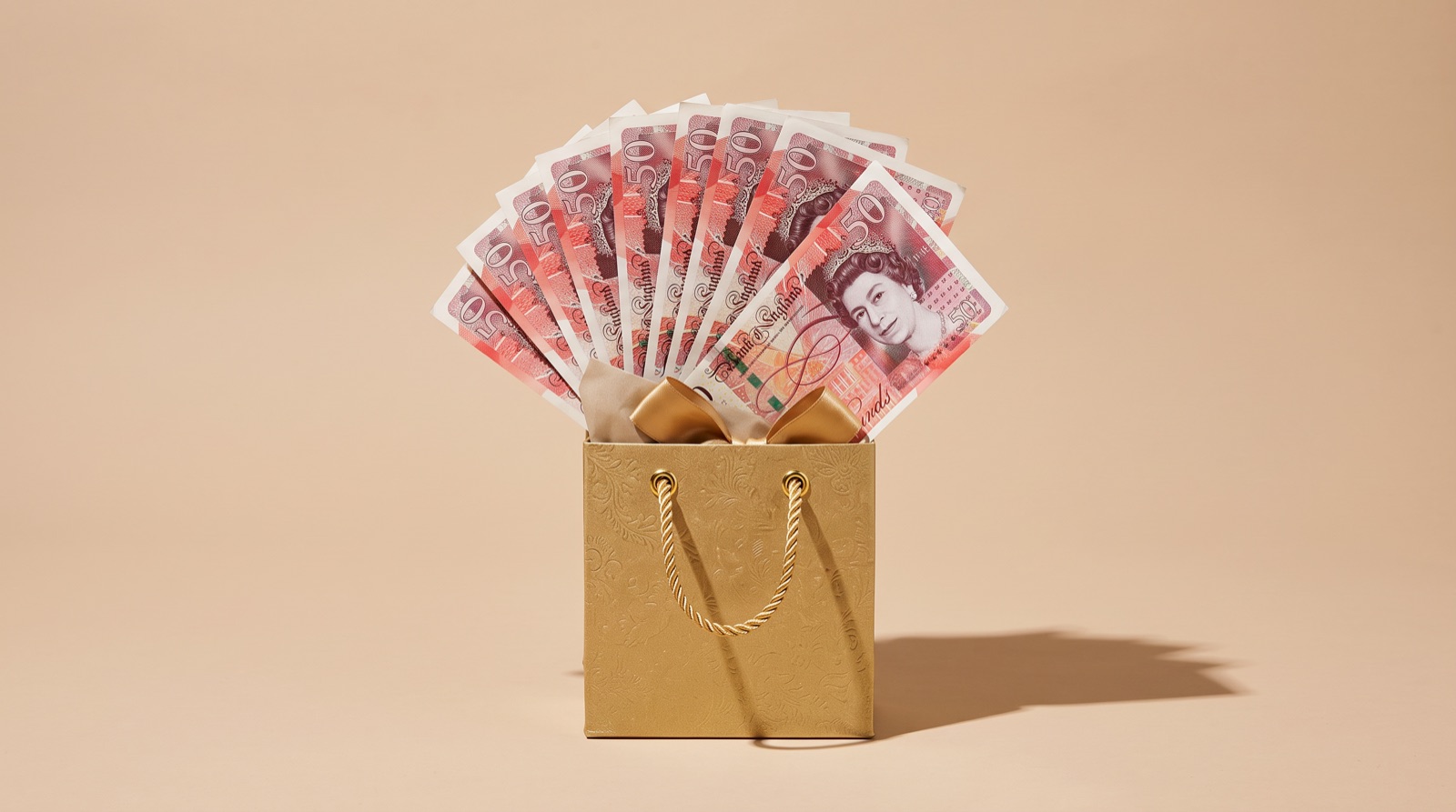 Gold gift bag filled with fanned £50 notes, representing a gifted house deposit from family