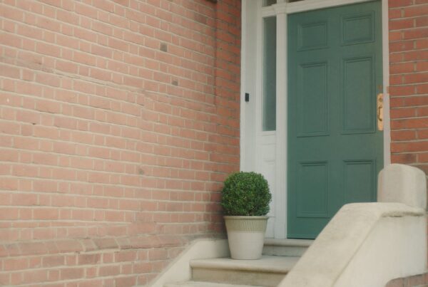 A Victorian red-brick mansion block entrance with a sage green front door, stone steps and a clipped box plant