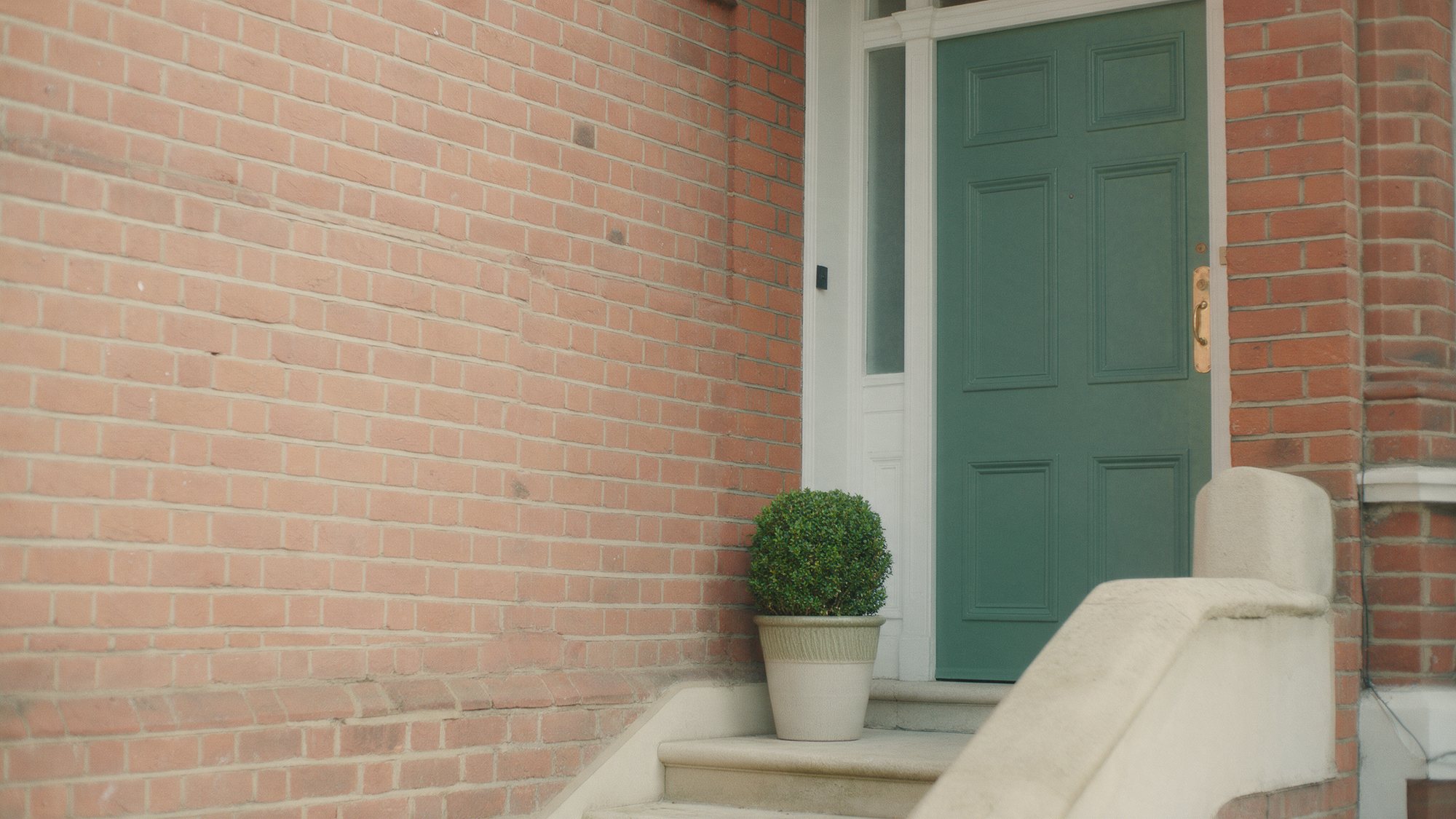 A Victorian red-brick mansion block entrance with a sage green front door, stone steps and a clipped box plant