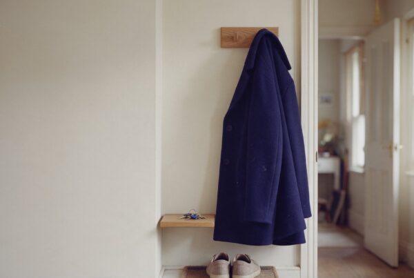 A navy wool coat hanging on an oak peg in the hallway of a UK home, with house keys on a small shelf