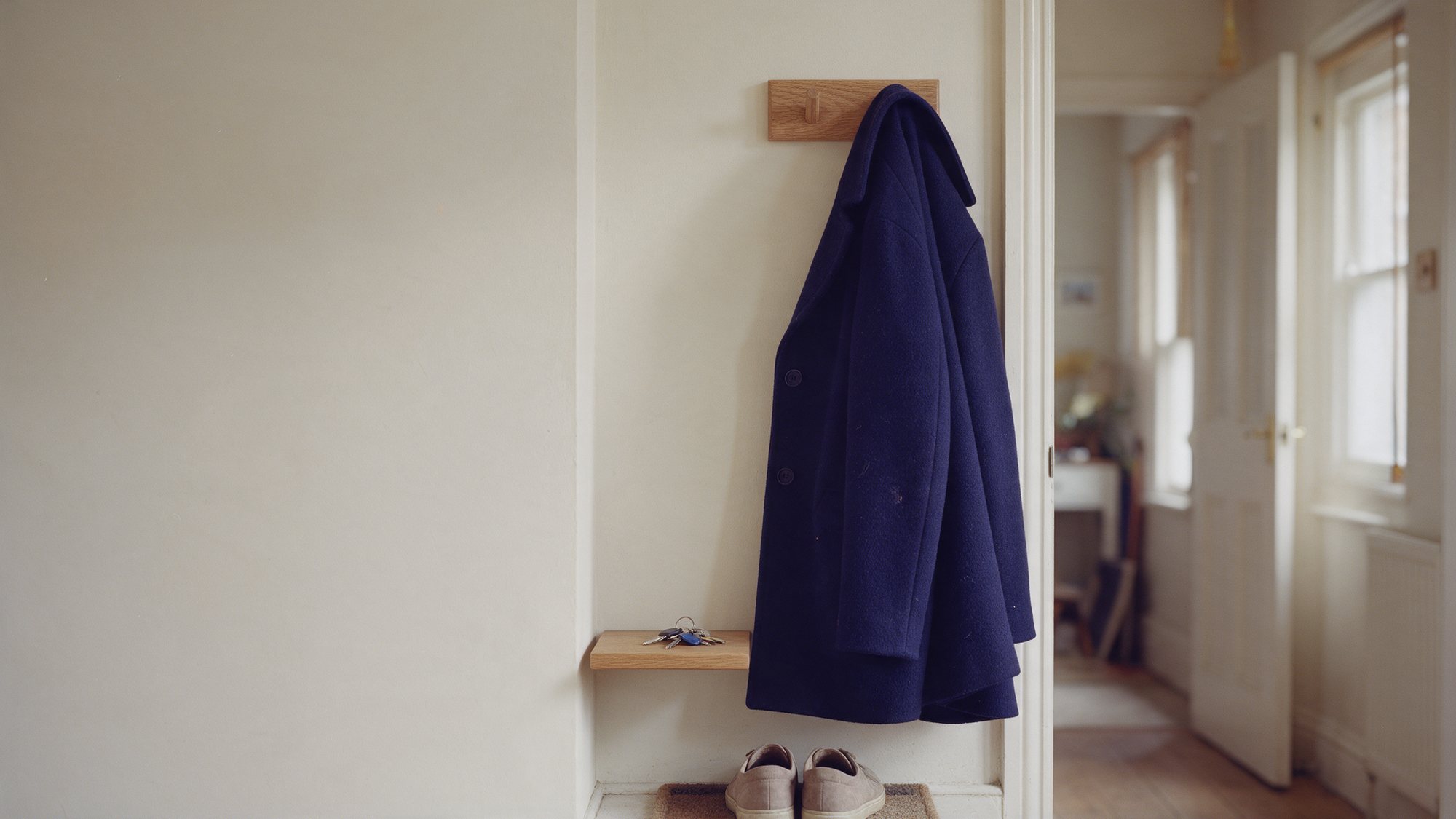 A navy wool coat hanging on an oak peg in the hallway of a UK home, with house keys on a small shelf